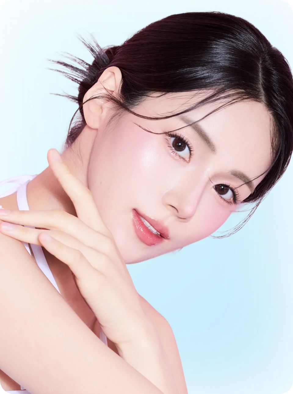 明るい背景の前に、髪をまとめた女性が肌に触れ、微笑んでいる。