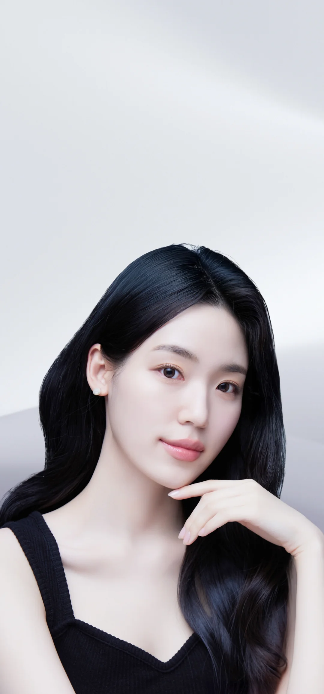 黒髪の女性が顎に手を当てて微笑んでいる、糸リフトのイメージ。